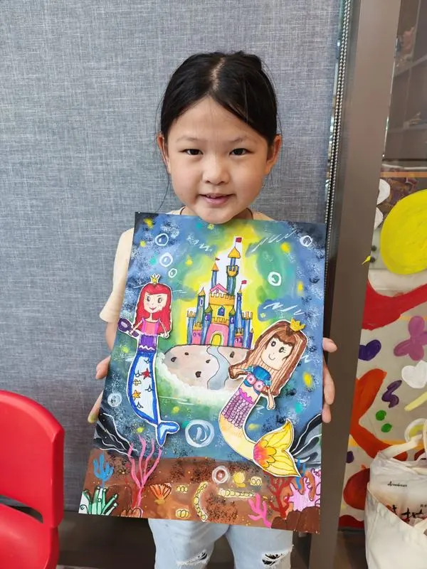 Girl holding vibrant mermaid and underwater castle painting from Art Journey workshop