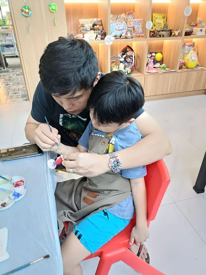Father holding young son on his lap while painting a figurine at Art Journey Singapore