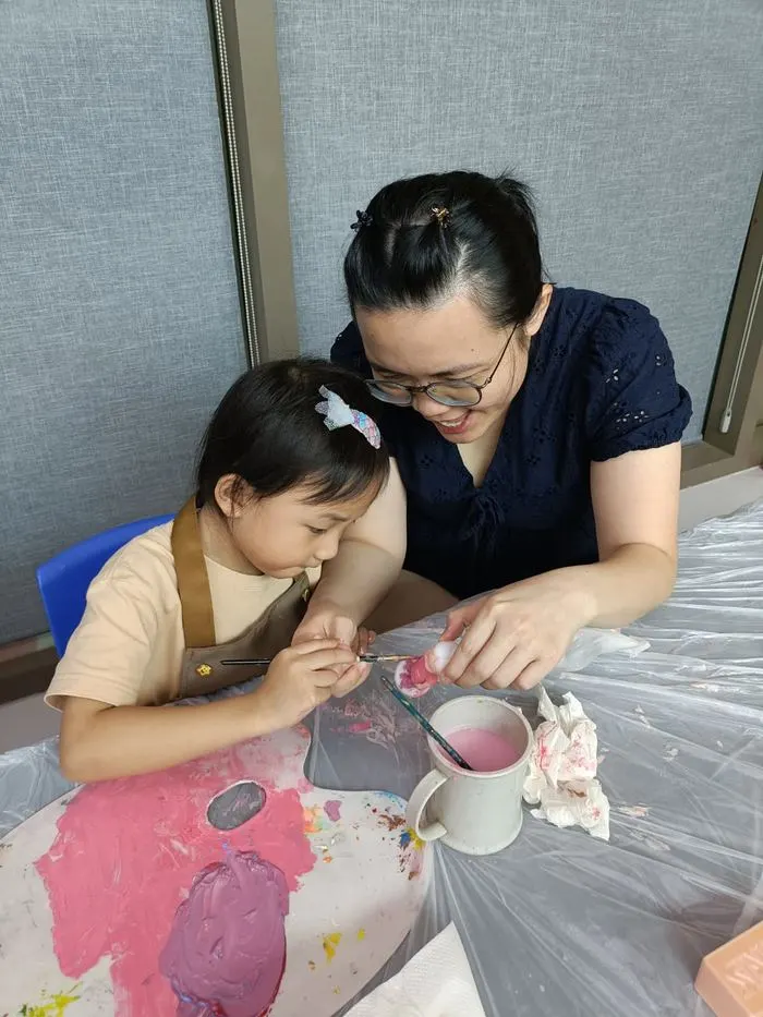 Mother and young daughter painting figurines together with Art Journey studio artwork display visible in background