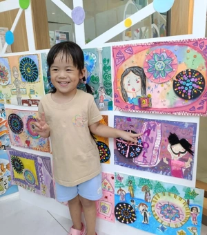 Happy young artist posing beside her artwork display at Art Journey kids art workshop in Singapore