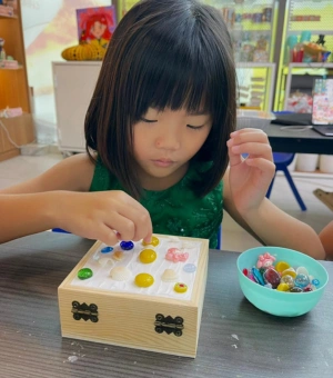 Young girl decorating a wooden jewellery box with gems and shells at Art Journey Singapore