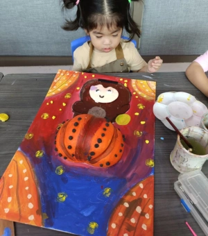 Toddler with a colourful mixed-media pumpkin painting at Art Journey kids art workshop in Singapore