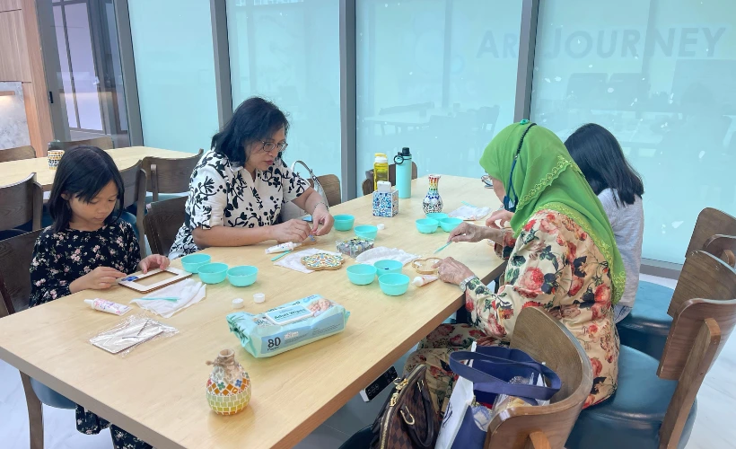 Grandfather and grandchild working on mosaic art together at Art Journey Singapore concentrating and creating