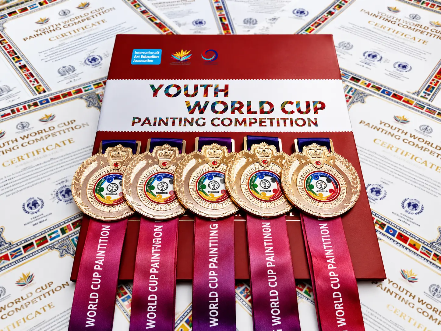 Youth World Cup Painting Competition medals laid out over printed award certificates