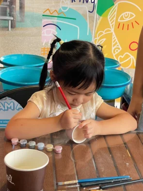 Child sketching her design before painting a ceramic cup