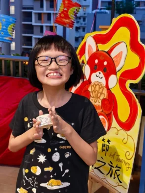 Girl smiling with the ceramic cup she painted at Art Journey